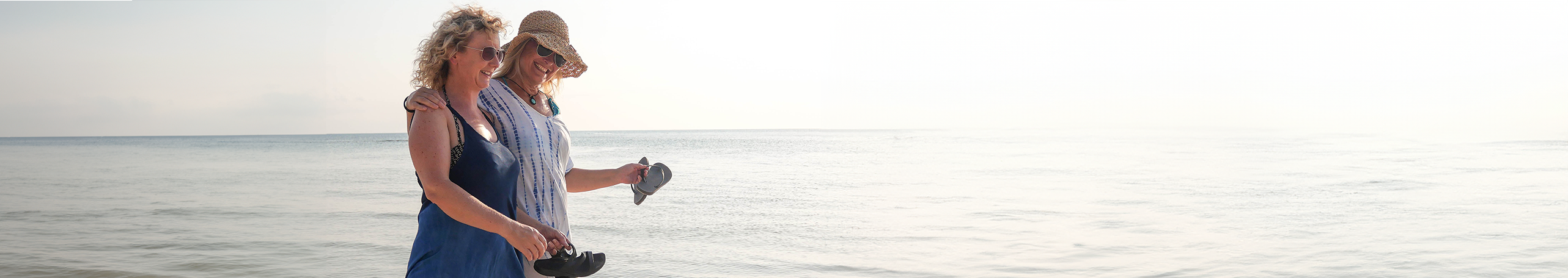 Two happy, empowered women in their 50s walking on the beach, possibly discussing a BreastScreen appointment.